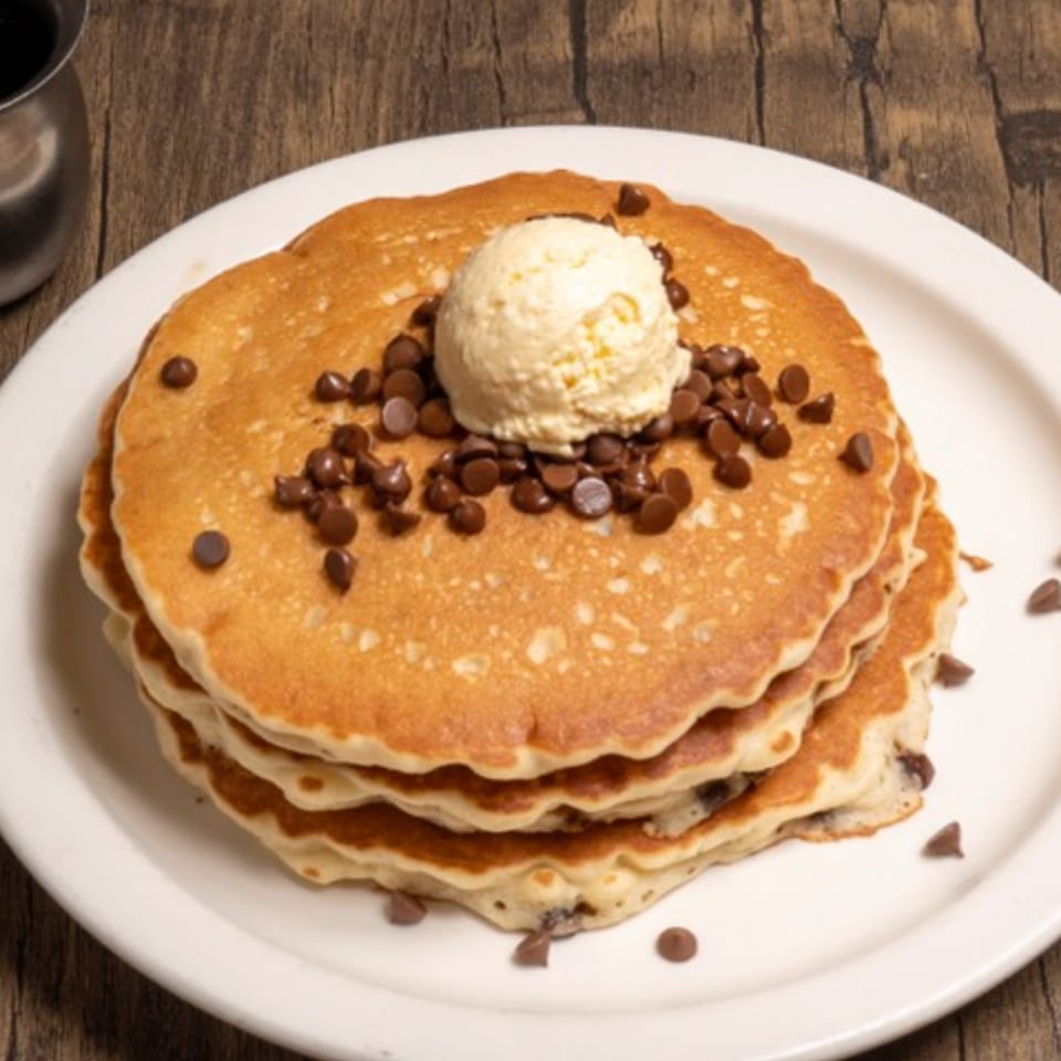 Stack of chocolate chip pancakes topped with a scoop of vanilla ice cream on a white plate.