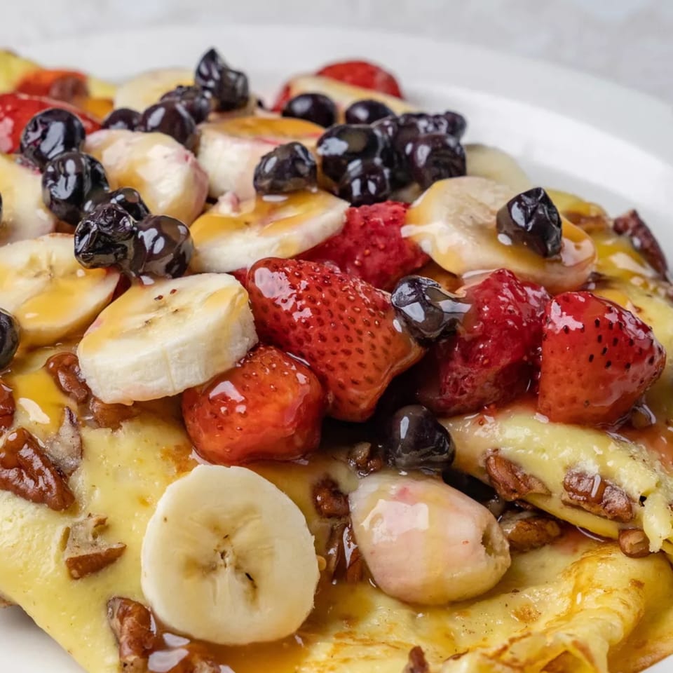 Close-up of Louie's Waffle House crepes topped with fresh strawberries, blueberries, bananas, and syrup.