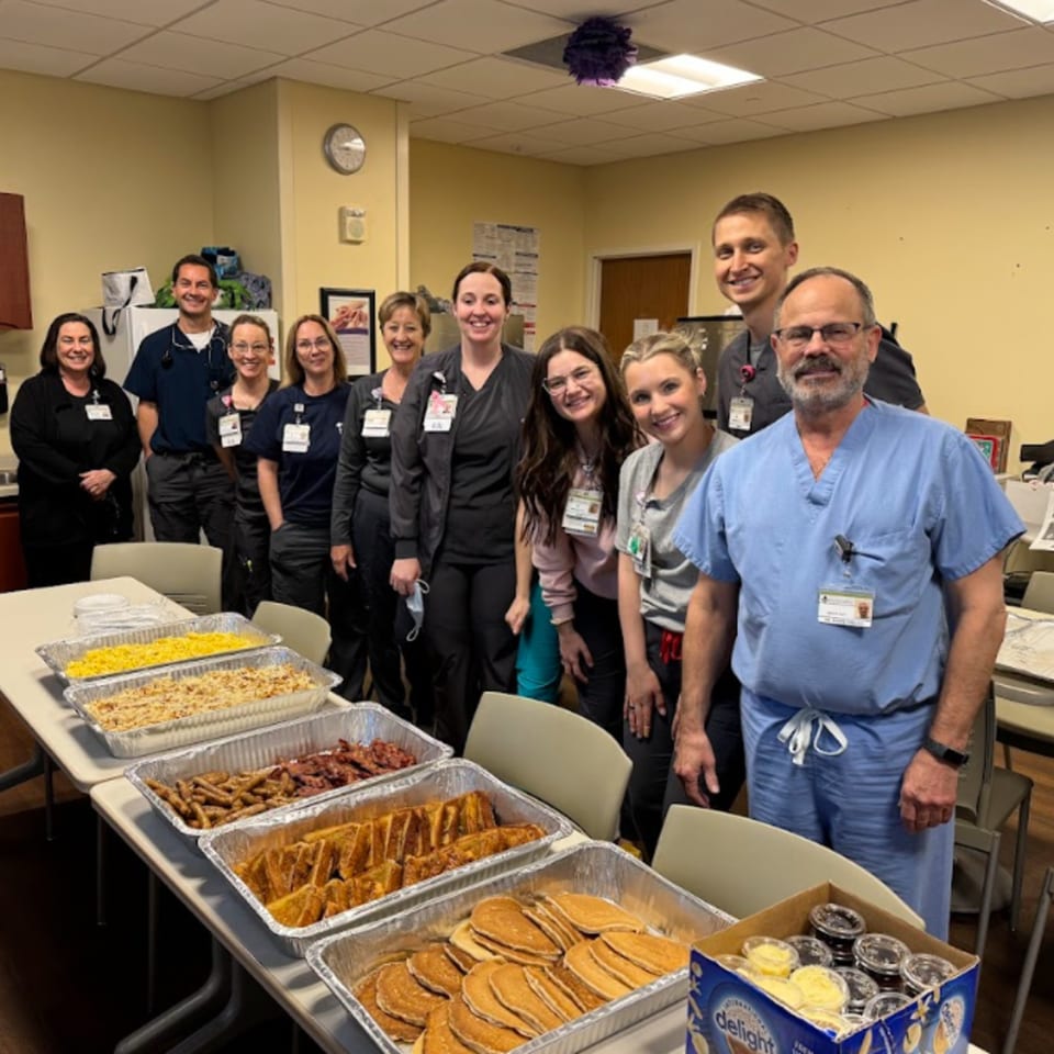 Medical staff smiling behind a table laden with Louie's Waffle House breakfast items like pancakes, French toast, and bacon.