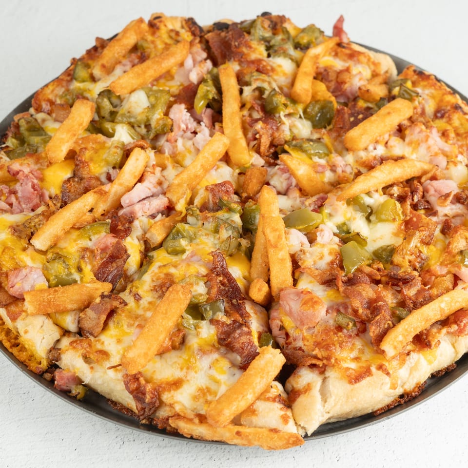 A Louie's Waffle House breakfast pizza topped with ham, bacon, green peppers, cheese, and french fries.