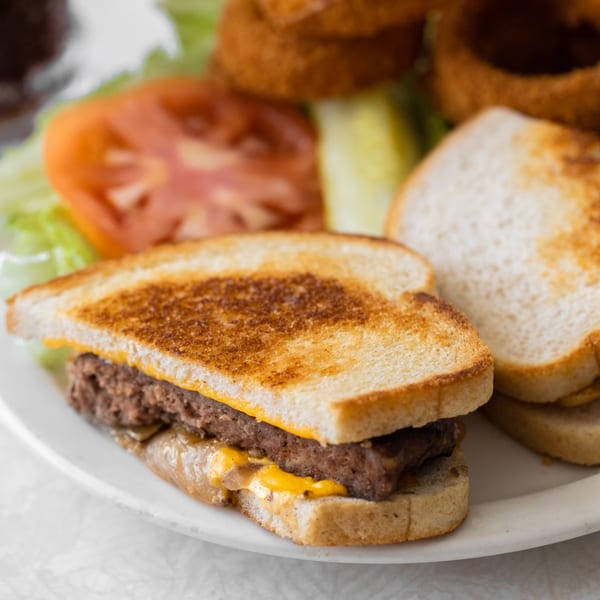 Louie's Waffle House patty melt with melted cheese, grilled onions, and toasted bread, served with onion rings.