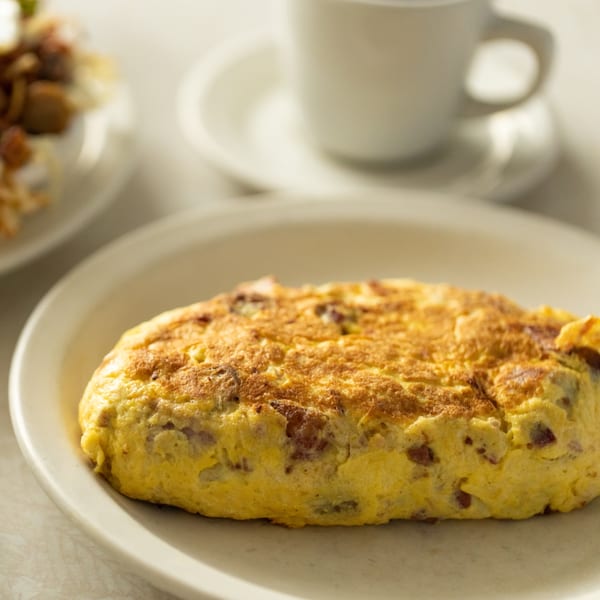 A golden-brown omelet with visible fillings on a white plate, with a coffee cup in the background.