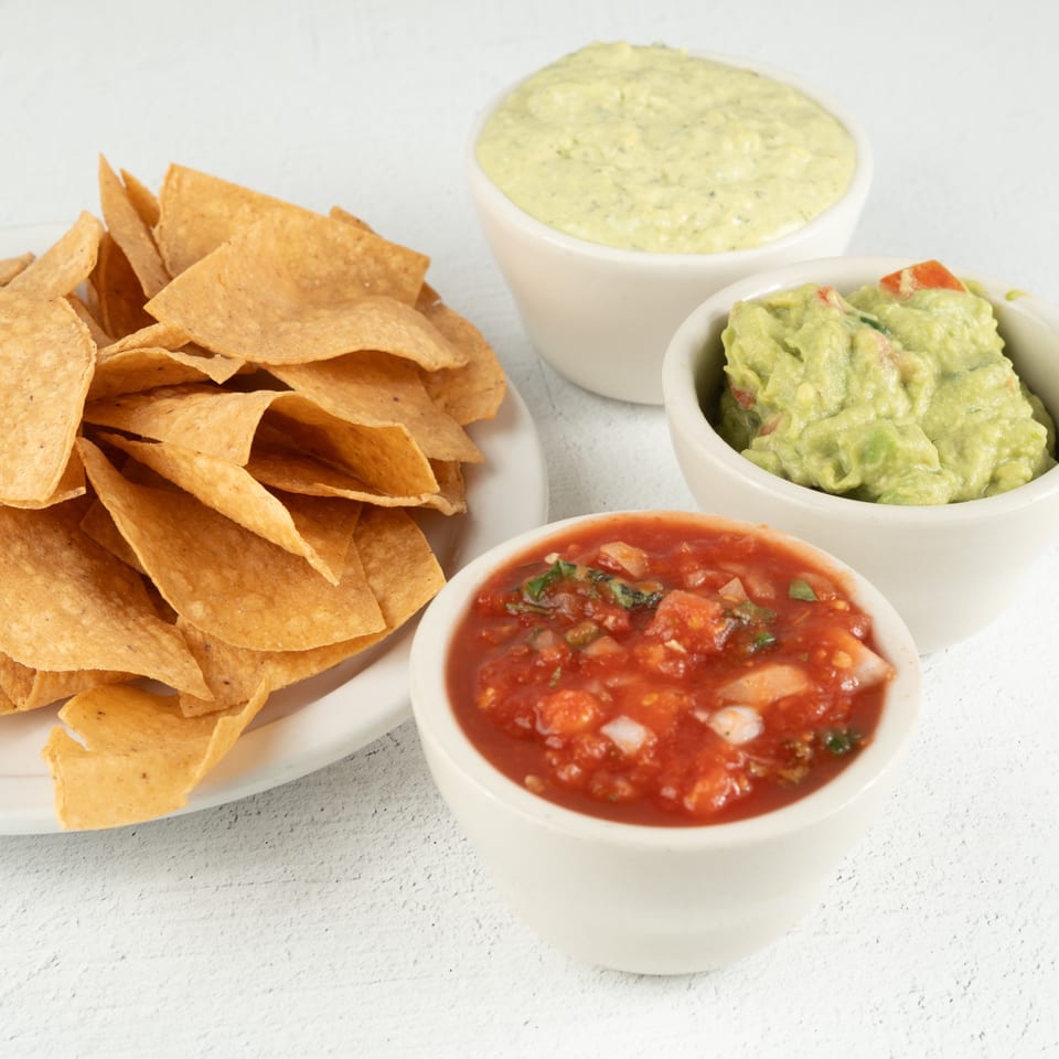 A plate of tortilla chips with bowls of salsa, guacamole, and a creamy green dip.