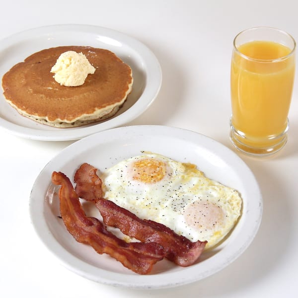 Louie's Waffle House breakfast with pancakes, bacon, fried eggs, and a glass of orange juice.