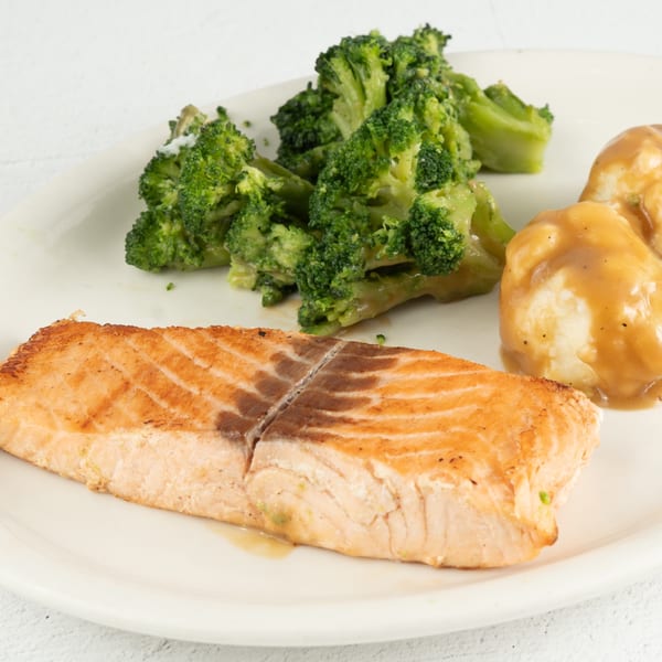 Grilled salmon fillet with a side of steamed broccoli and mashed potatoes with gravy.