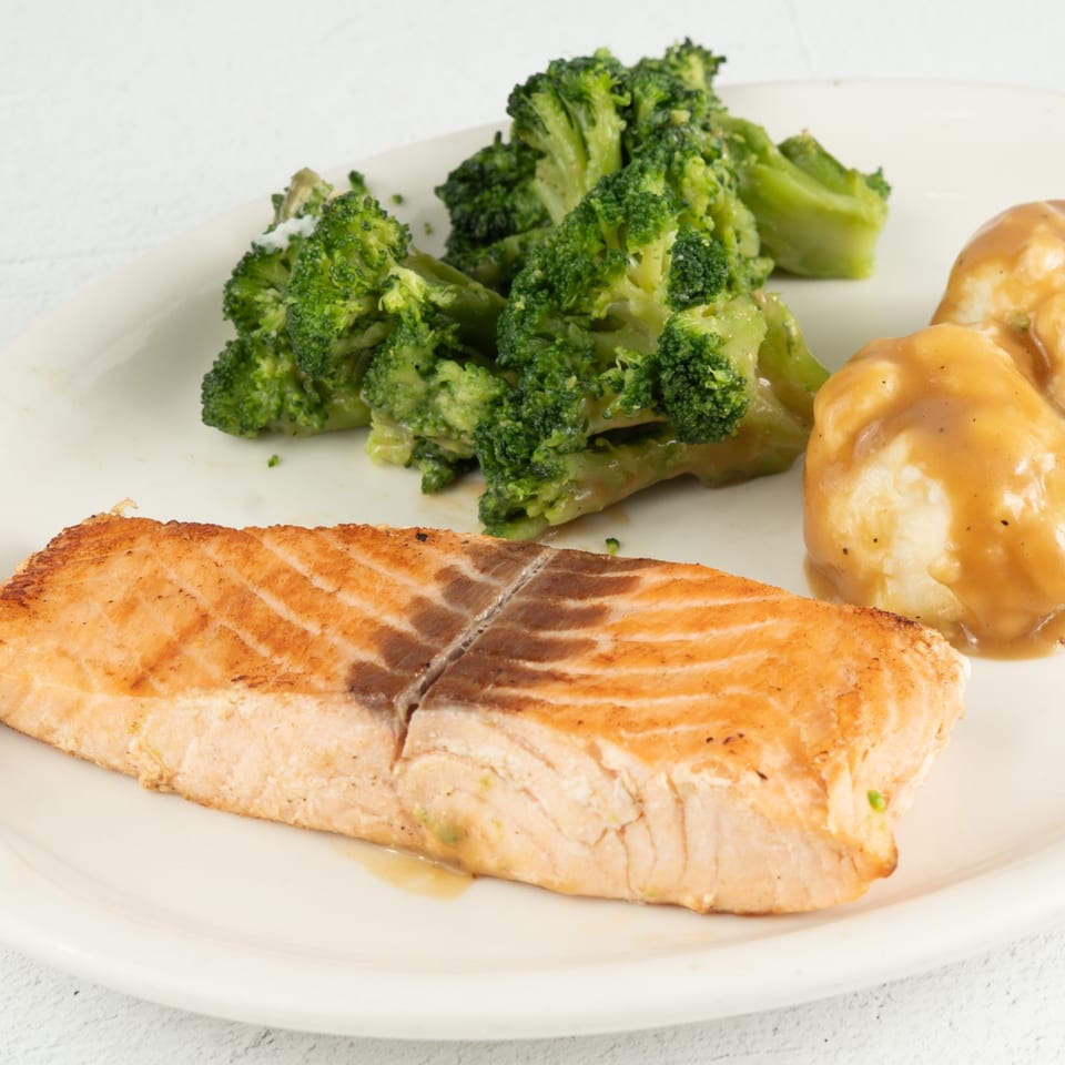 Grilled salmon fillet with a side of steamed broccoli and mashed potatoes with gravy.