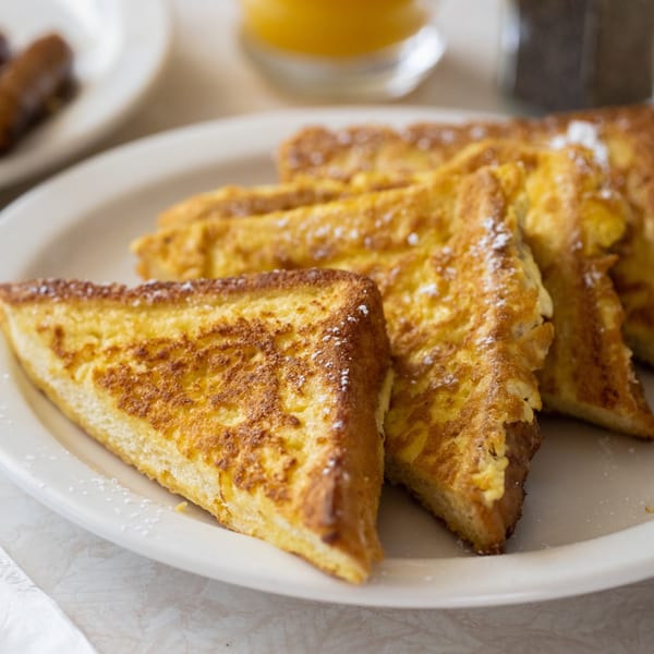 Golden brown French toast triangles dusted with powdered sugar on a white plate at Louie's Waffle House.