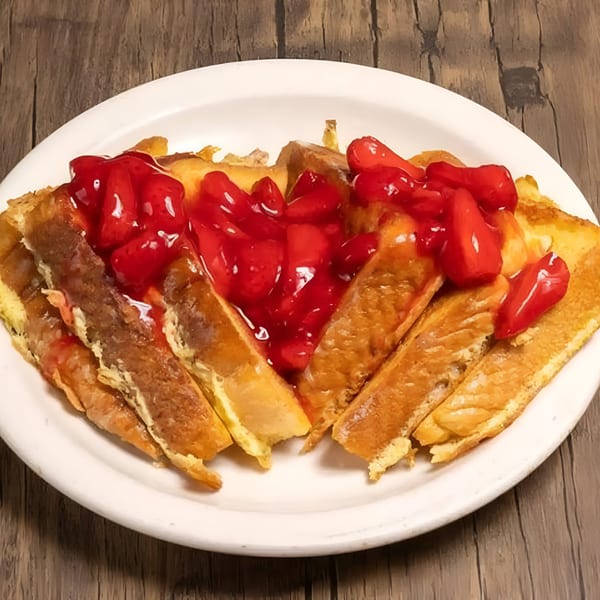 Golden French toast sticks covered with bright red strawberry topping on a white plate.