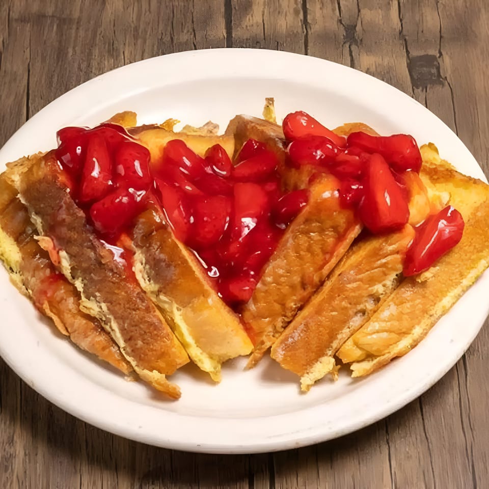 Golden French toast sticks covered with bright red strawberry topping on a white plate.