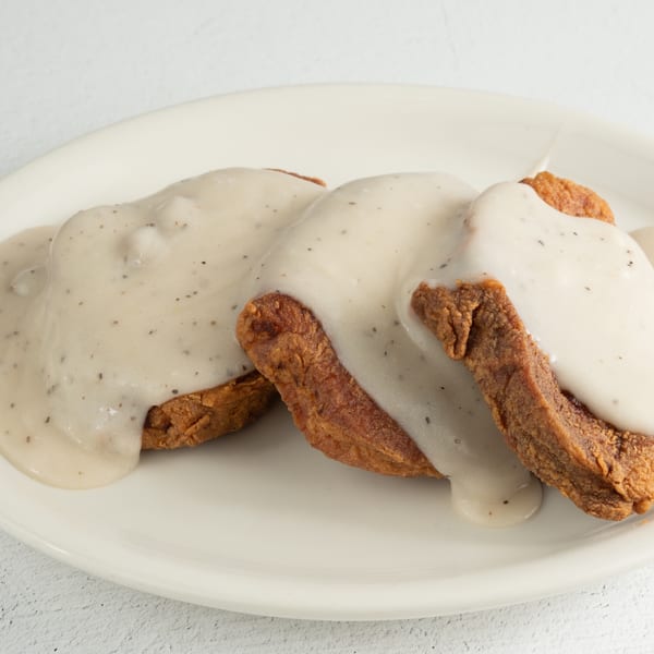 Three pieces of golden-brown chicken fried steak covered in creamy white gravy with pepper flakes.