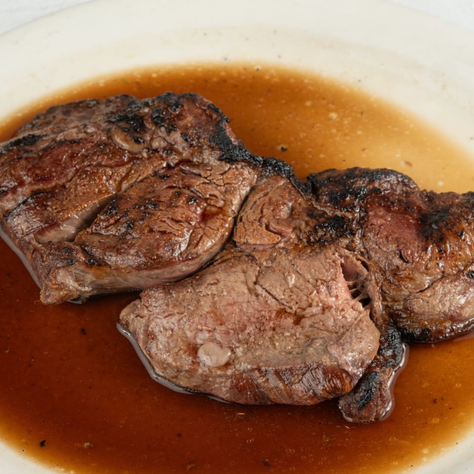 Grilled steak with a rich brown sauce, served on a white plate at Louie's Waffle House.