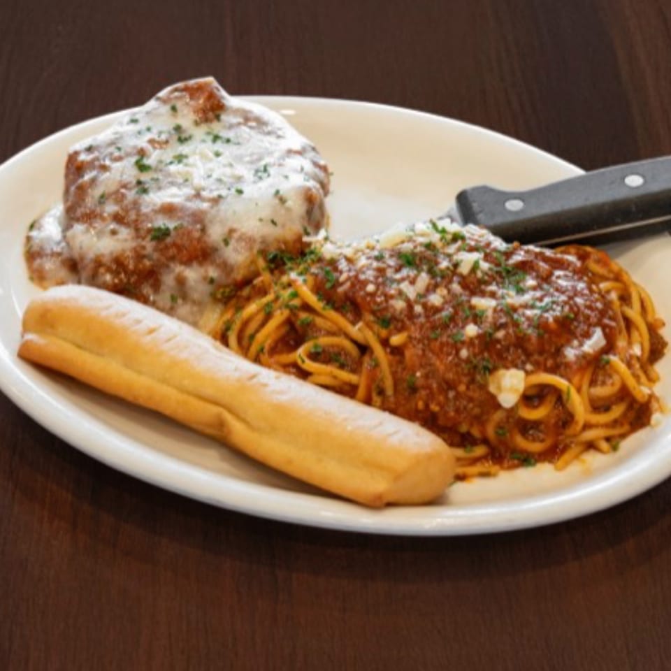 Spaghetti with meat sauce, a large meatball with white sauce, and a breadstick on a white plate.