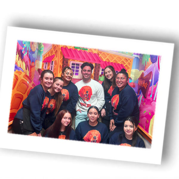 Nine Louie's Waffle House staff members pose in front of a colorful, waffle-themed mural.