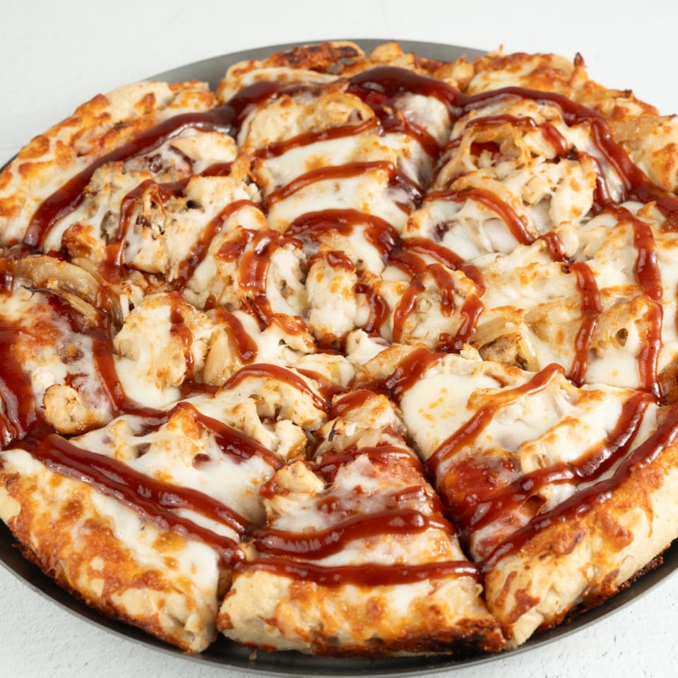 Close-up of a BBQ chicken pizza with melted cheese and sauce, sliced and ready to eat.