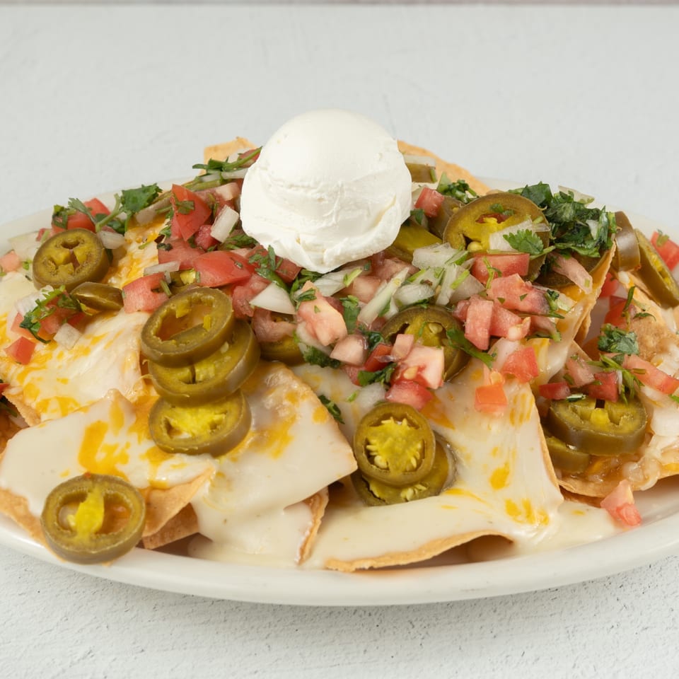 A plate of nachos with melted cheese, jalapeños, pico de gallo, and a dollop of sour cream.