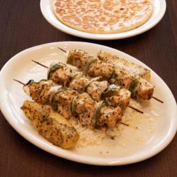 Chicken and vegetable skewers with rice and potatoes, with a flatbread in the background.