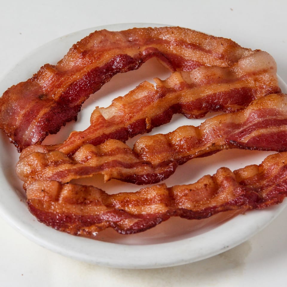 Crispy strips of bacon, perfectly cooked, arranged on a white plate at Louie's Waffle House.