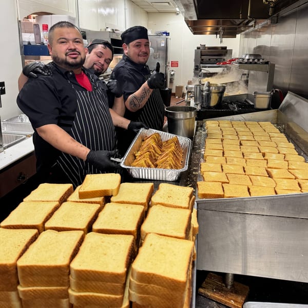 Three Louie's Waffle House chefs in a busy kitchen preparing large quantities of French toast.