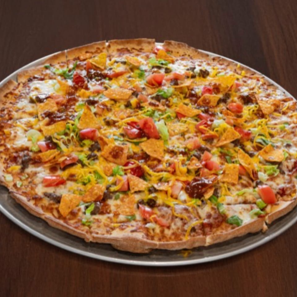 A large pizza topped with ground meat, cheese, tomatoes, lettuce, and tortilla chips.
