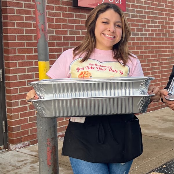 Smiling Louie's Waffle House employee in a pink shirt and apron holding two catering trays.