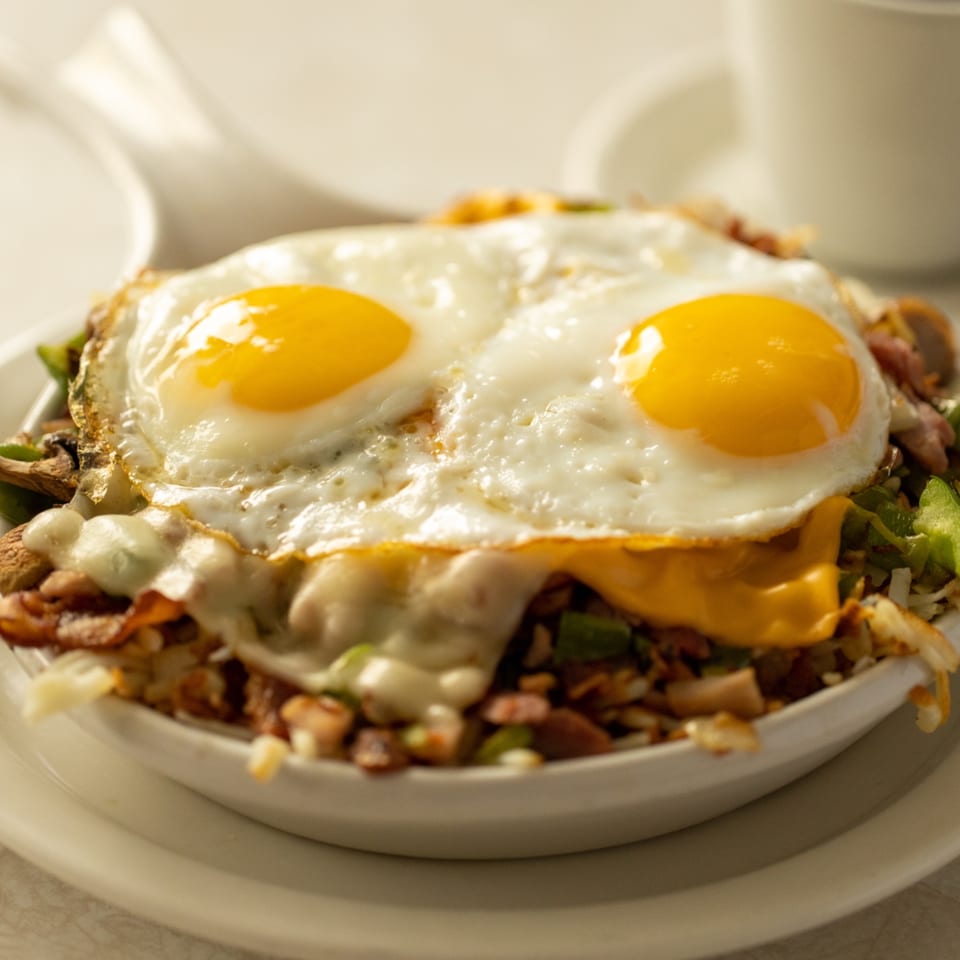 A breakfast skillet from Louie's Waffle House, topped with two fried eggs and melted cheese.