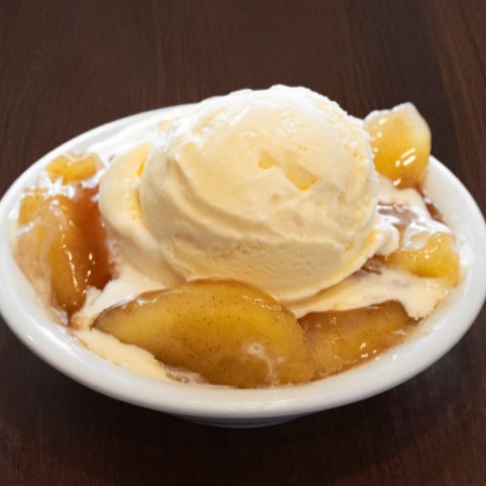 A white bowl filled with vanilla ice cream and warm cinnamon-spiced apples on a dark wooden table.