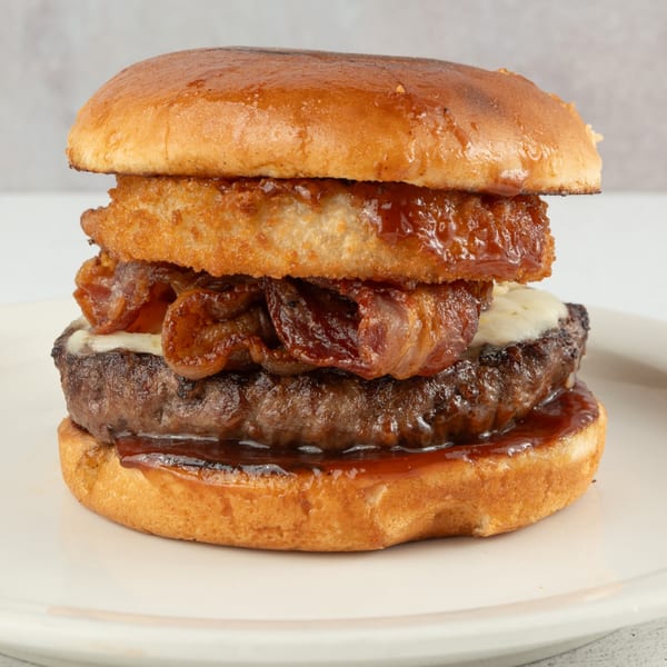 A Louie's Waffle House burger with bacon, cheese, and onion rings on a white plate.