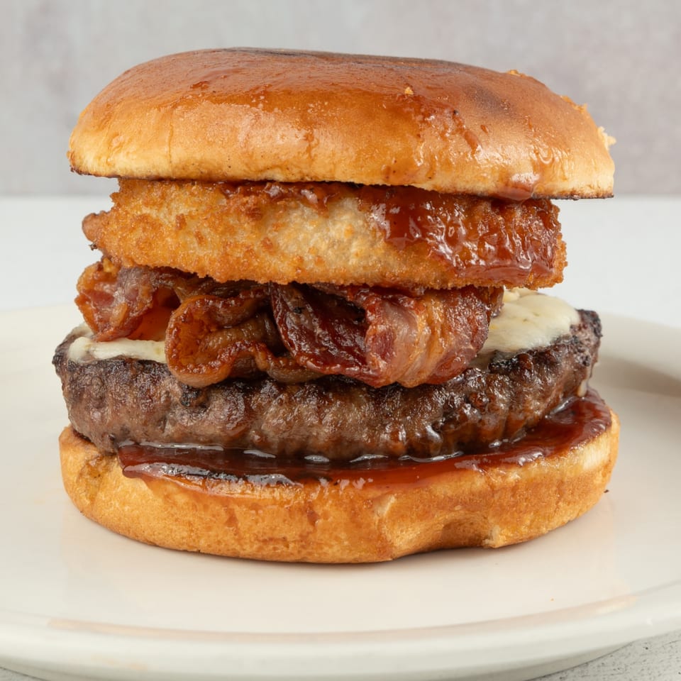 A Louie's Waffle House burger with bacon, cheese, and onion rings on a white plate.