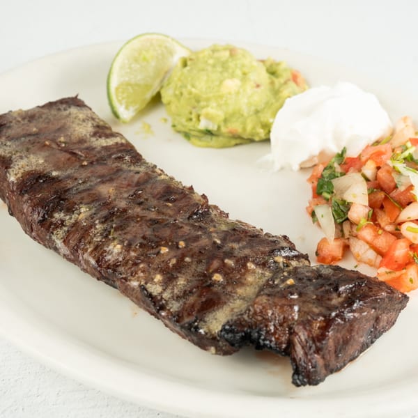 Grilled skirt steak with a side of guacamole, sour cream, pico de gallo, and a lime wedge.